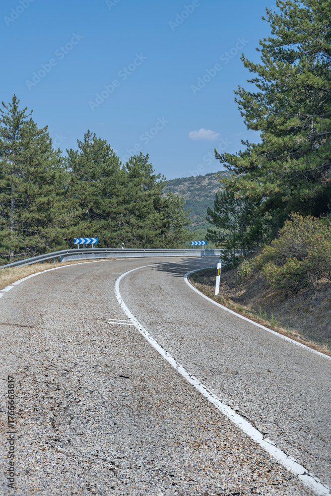 Fototapeta premium Mountain road with banked curves descends between terraces. Natural terraced vegetation and eroded rock formations