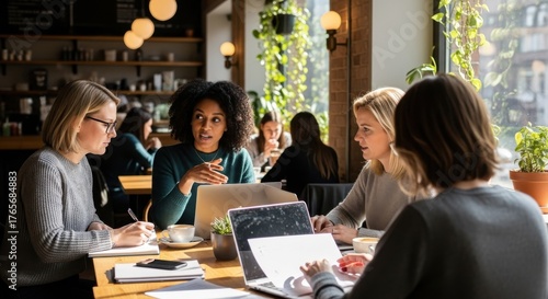 Four diverse businesswomen having a meeting in a modern cafe. Female colleagues brainstorming, discussing a project and working on laptops. Teamwork, collaboration and startup concept.