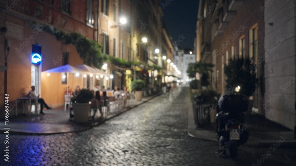 Fototapeta premium Night cobblestone street with cafe terraces and parked scooter, defocused bokeh street; background backdrop copyspace.