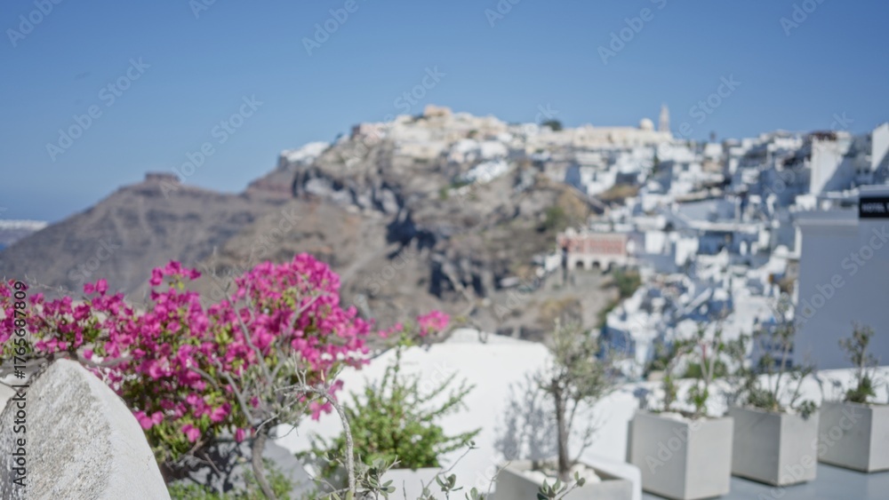 Fototapeta premium Pink bougainvillea foreground and white hillside village on sunlit cliffs in soft bokeh outdoor; background backdrop copyspace calm.