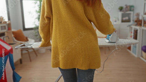 Photography Woman ironing in a cozy laundry room with modern decor, wearing a yellow sweater, surrounded by household items indicating a warm home environment, focused on cleaning tasks