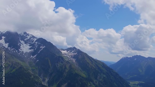 Majestic Mountain Peaks with Snow and Lush Greenery Under a Cloudy Blue Sky.