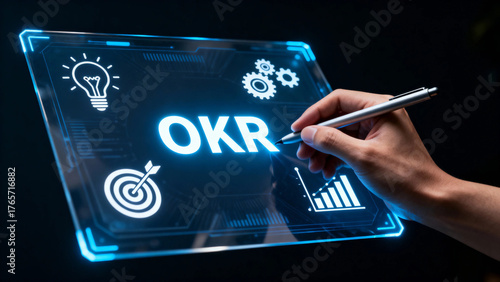 Hand writing OKR on a futuristic digital tablet with icons representing goals, innovation, and analytics
