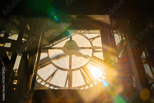 Sunlit view of clock tower interior with beams of light streaming through glass face creating warm glow. Clock tower