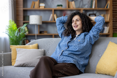 Photos Young happy woman with curly hair relaxing on a comfortable sofa in her living r