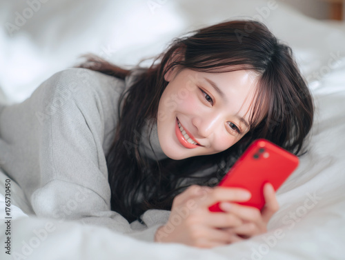 ベッドで赤いスマートフォンを見て明るい笑顔を見せる美しい若い女性のリラックスした瞬間