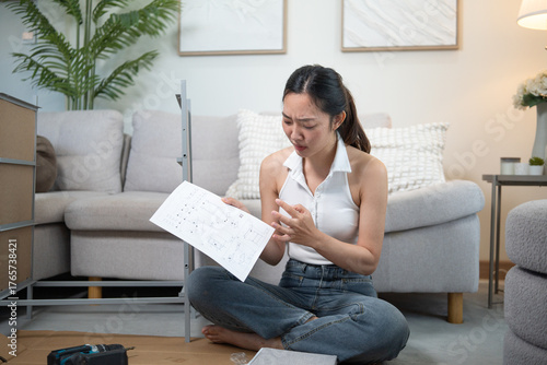 Young woman sitting on the floor looking puzzled while reading assembly instructions during a DIY furniture project.