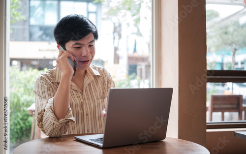 Young man having a phone conversation while working on a laptop in a cafe.
