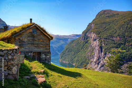 Historic Skagefla farm above Geirangerfjord with Seven Sisters Waterfall visible across the fjord in Norway