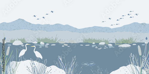 Two elegant white egrets stand by a calm blue lake with distant mountains and birds flying in the sky