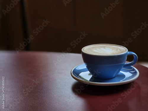 blue coffee cup with latte art sits on red table, creating cozy atmosphere. warm tones invite relaxation and enjoyment of delicious beverage