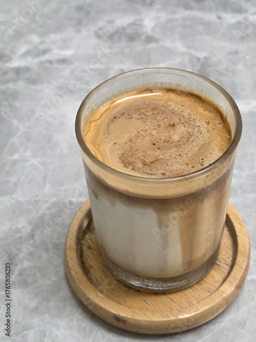 delicious layered coffee drink served in clear glass, showcasing rich espresso and creamy milk on wooden coaster. Perfect for coffee lovers