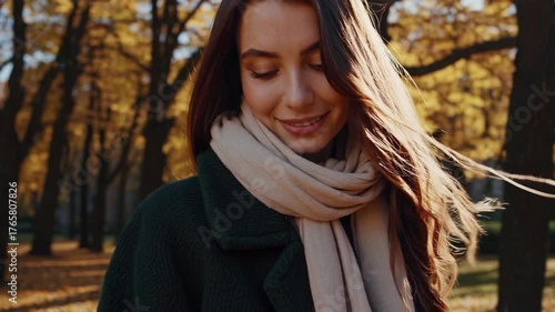 Caucasian woman walking in park filled with golden autumn leaves. She smiles softly as her hair flows in the breeze, enjoying the serene atmosphere of nature.