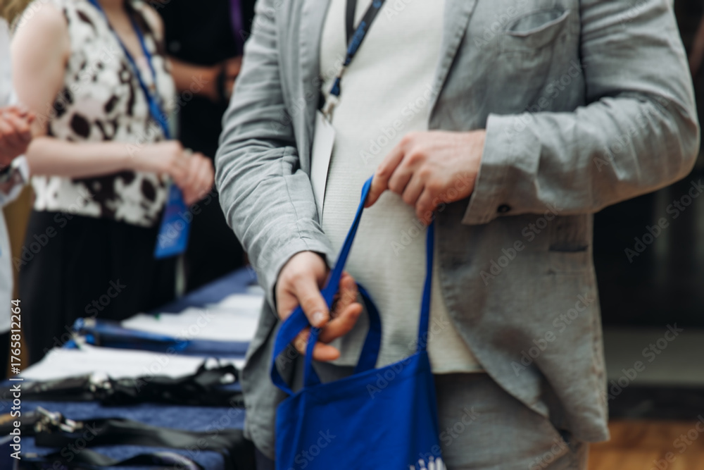 Fototapeta premium Process of checking in on conference congress forum event, registration desk table, visitors and attendees receiving lanyard with name badge and entry wristband bracelet and register electronic ticket