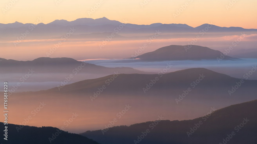 Fototapeta premium Serene mountain peaks shrouded in soft morning mist under a warm golden sunrise sky