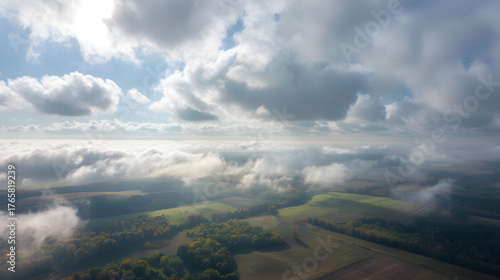 Aerial drone view from above the clouds over a rural landscape. Foggy autumn countryside with fields and forests. Bird's eye perspective of nature