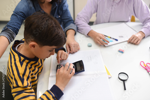 Ten-year-old boy doing math homework with calculator beside his mother and sister at home
