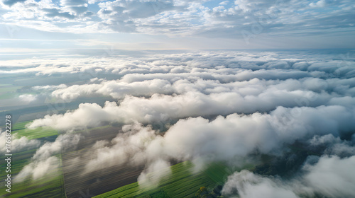 High altitude aerial view from a drone flying over a sea of clouds. Bird's-eye perspective of a rural landscape with green agricultural fields below