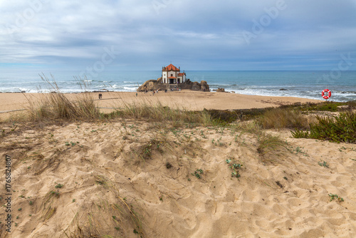 Fototapeta Naklejka Na Ścianę i Meble -  A sandy beach with dune grass in the foreground leads to a historic chapel