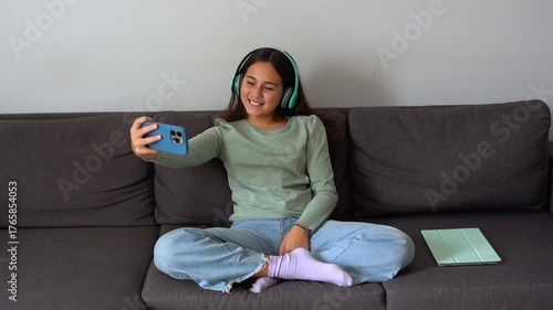 Teenager girl using smartphone and wireless headphone taking a selfie at home - Childhood, technology and addiction concept 