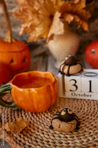 Traditional fall Halloween still life - cookies in shape of spider and cup of tea among pumpkins and Jack o lantern. 31 of October on calendar