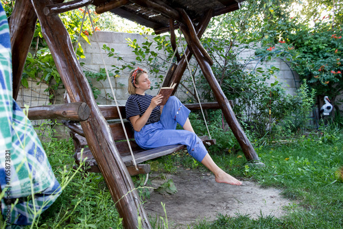 teenage girl sitting on swing, reading a book, headband, blonde, barefoot, wooden swing, summer, woman, profile

