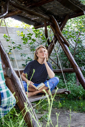 teenage girl sitting on  swing,  book on her bare feet, blonde, looking into frame, smiling, 