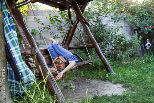 teenage girl lying on a swing, a book on her face, blonde, bare feet on the back, a headband on her head, wooden swing, summer, woman, 
