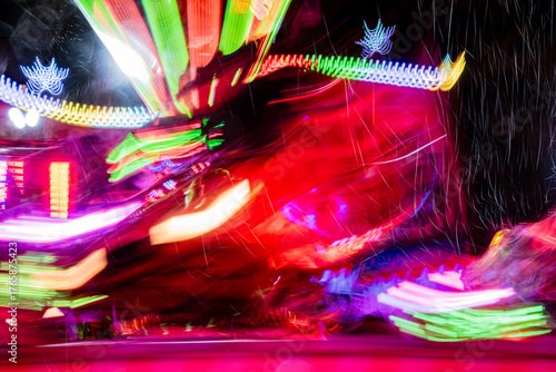 Bewegliche Lichter eines Karussells mit bunter Beleuchtung. Verschwommene Lichtspuren und -flecken, aufgenommen mit Langzeitbelichtung auf einem Jahrmarkt in Deutschland