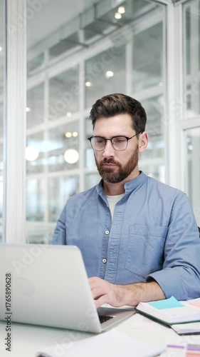 Thoughtful businessman working on laptop sitting at desk at workplace in business office. Manager thinking about problem solving, engaged in a task or is busy with project on computer. Vertical video