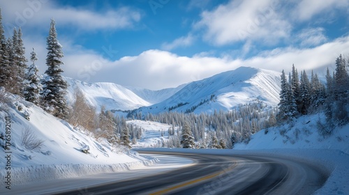 Snow-covered mountain road winding through winter landscape in a serene, sunny day with clouds and blue sky above