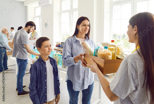 Quadro su tela Group of volunteers working at charity center giving free food donations for woman with child boy in need in charitable foundation