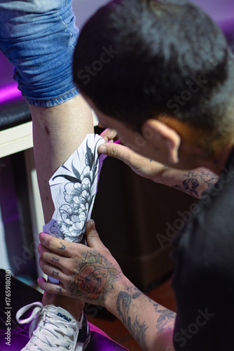 Tattoo artist preparing design, applying temporary stencil drawing on leg, creating body art