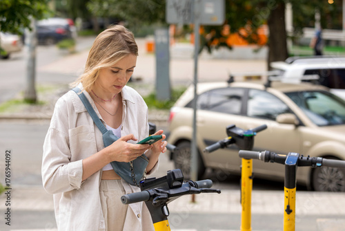 woman using smartphone while standing near electric scooter on city street