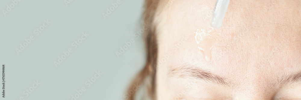 Naklejka premium Female applying skincare serum to forehead with dropper on clear background.