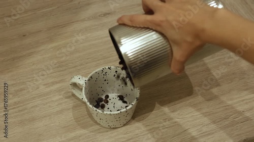 A person pouring coffee beans from a container into a small cup. The action highlights the process of preparing fresh coffee.