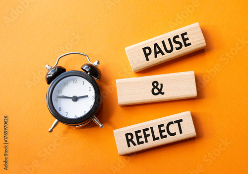 Pause and Reflect symbol. Concept words Pause and Reflect on wooden blocks. Beautiful orange background with alarm clock. Business and Pause and Reflect concept. Copy space.