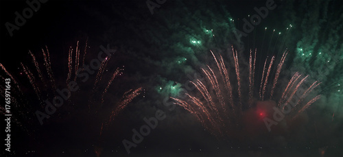 dynamic fireworks burst mixing green and red spark trails in the dark sky.
