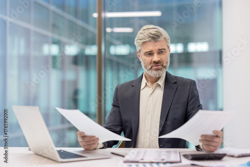 Obraz na płótnie Confused senior businessman comparing financial reports, analyzing data, and fin