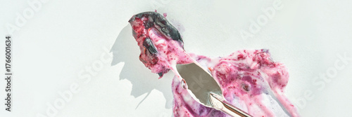 Melting berry ice cream on white background with metal ice cream scoop revealing texture.