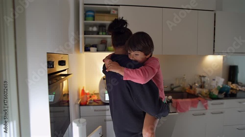 Mother holding young child in cozy kitchen, child resting quietly on her shoulder with affectionate gaze, capturing tenderness, care, and the warmth of everyday family life