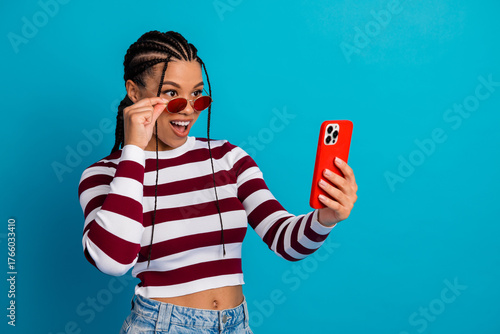 Foto Young stylish woman smiles at her phone wearing a striped top and red sunglass a