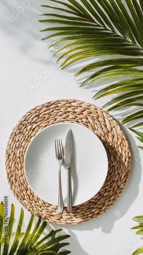Elegant Dining Setup With White Plate and Cutlery Surrounded by Green Palm Le...