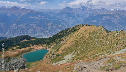 Mountain landscape with alpine Chamole lake, enclosed within a green basin, which provides a excellent panorama of Aosta valley. Turquoise color of the lake. Famous hiking trail above the lake.