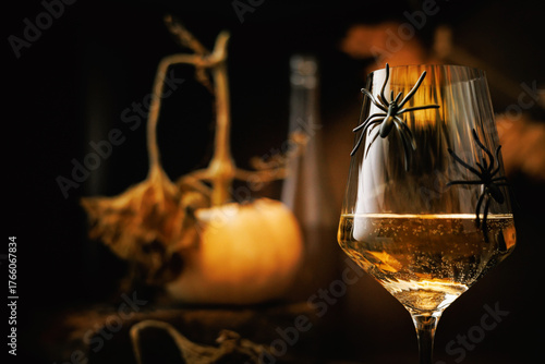 Glass of white wine with spiders in front of dried pumpkin stem and bottle in moody Halloween composition