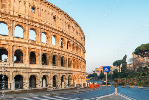Fototapeta Naklejka Na Ścianę i Meble -  Side view of ancient Roman Colosseum Amphitheater in Rome city, Italy at sunrise with empty streets. Italian architecture. Popular touristic and travel landmark