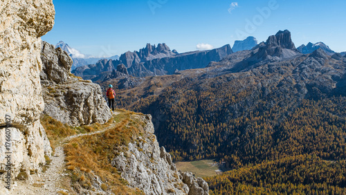 Girl with helmet and backpack admires the view from a mountain top with autumn colors in the Dolomites