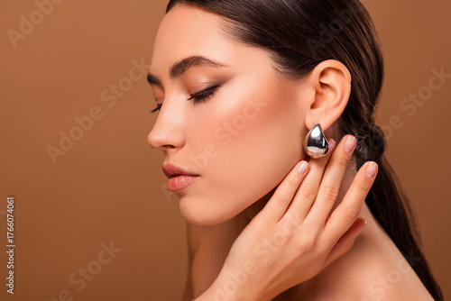 Sensual portrait of a young woman with sleek hairstyle, focusing on her flawless skin, wearing metallic earrings
