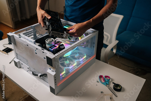 Unrecognizable computer technician installing new graphics card into modern custom-built pc with RGB lighting, enhancing gaming performance and visual experience, upgrading desktop PC.