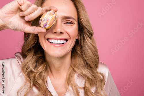 Smiling mature woman holding an artful object in front of her eye against a pink background